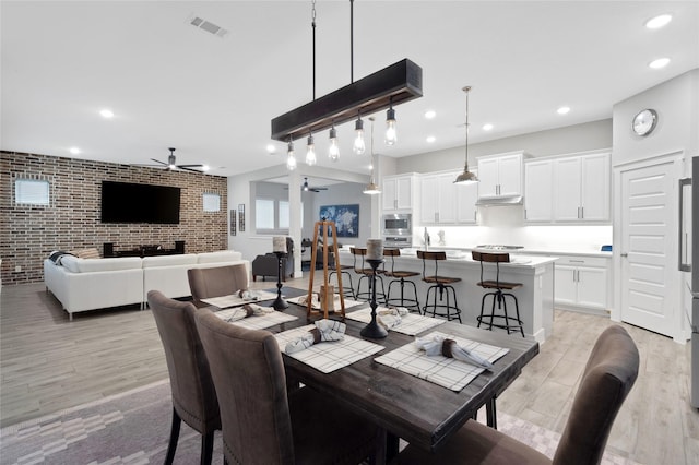 dining area featuring light wood-type flooring, ceiling fan, and brick wall