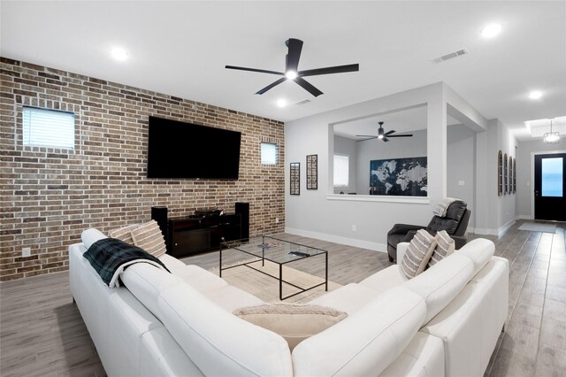 living room featuring light hardwood / wood-style floors, ceiling fan, and brick wall