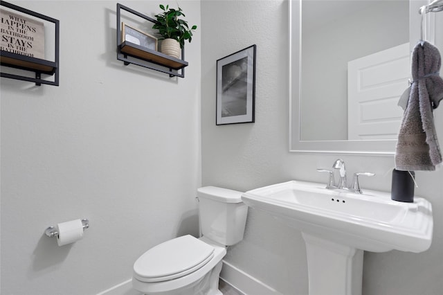 half bath with a sink, toilet, and baseboards