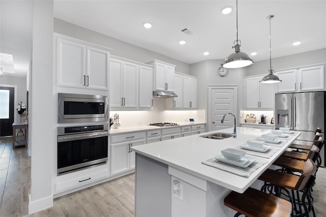 kitchen with appliances with stainless steel finishes, a center island with sink, decorative light fixtures, and sink