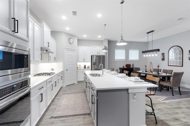 kitchen featuring a kitchen island with sink, stainless steel appliances, a breakfast bar, a sink, and light countertops