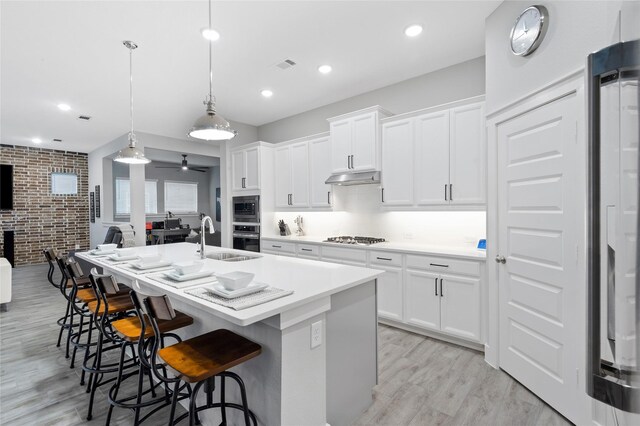 kitchen with white cabinets, hanging light fixtures, ceiling fan, an island with sink, and brick wall