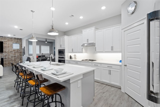 kitchen with a center island with sink, brick wall, appliances with stainless steel finishes, open floor plan, and a sink