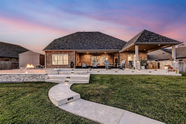 back house at dusk featuring a patio area and a lawn