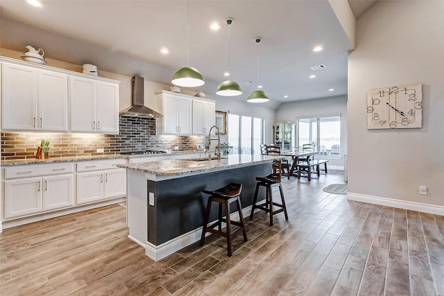 kitchen with a center island with sink, white cabinetry, and wall chimney range hood