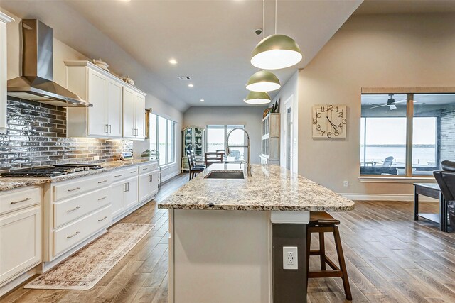 kitchen featuring decorative light fixtures, stainless steel gas stovetop, sink, a center island with sink, and wall chimney exhaust hood