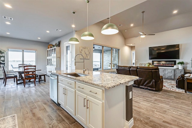 kitchen featuring sink, light stone counters, white cabinetry, hanging light fixtures, and a center island with sink