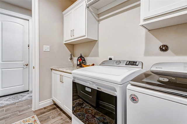 washroom with cabinets, washing machine and clothes dryer, and light hardwood / wood-style flooring