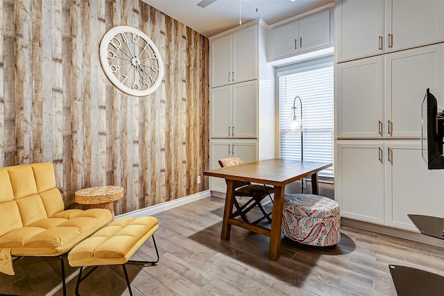 dining area with ceiling fan, wood walls, and light wood-type flooring