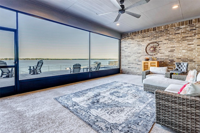 living room with a water view, ceiling fan, brick wall, and carpet