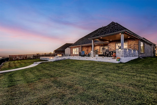 back house at dusk featuring a yard and a patio area