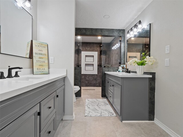 bathroom with toilet, vanity, tile patterned flooring, a textured ceiling, and a tile shower