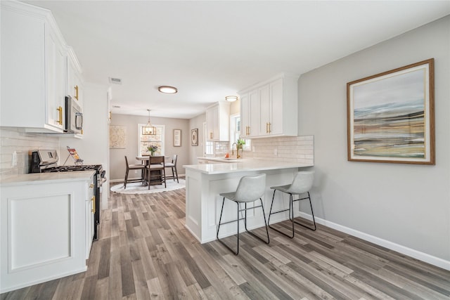 kitchen featuring a kitchen breakfast bar, kitchen peninsula, pendant lighting, white cabinetry, and white range with gas stovetop