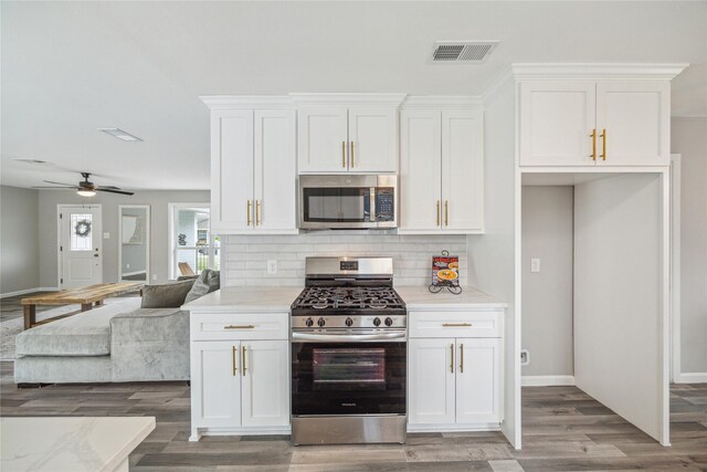 kitchen with hardwood / wood-style floors, appliances with stainless steel finishes, ceiling fan, white cabinets, and backsplash