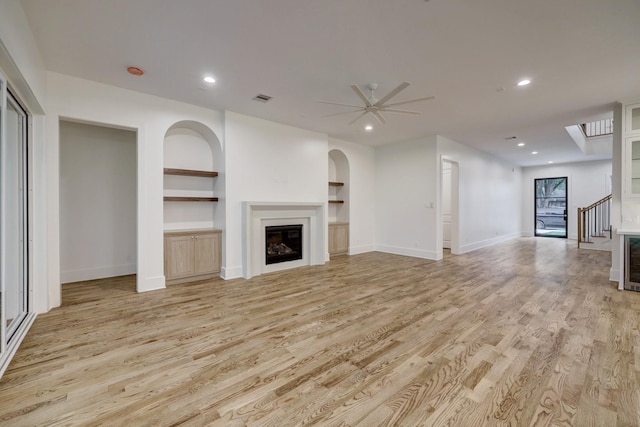 unfurnished living room featuring light wood-type flooring, built in features, and ceiling fan