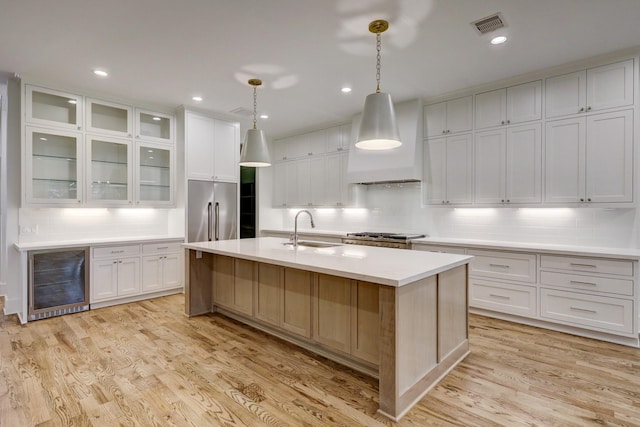 kitchen featuring a kitchen island with sink, sink, white cabinets, and hanging light fixtures