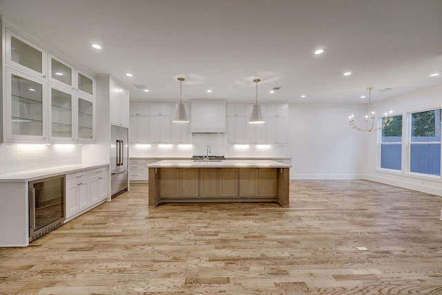 kitchen featuring a large island with sink, white cabinets, wine cooler, hanging light fixtures, and built in fridge