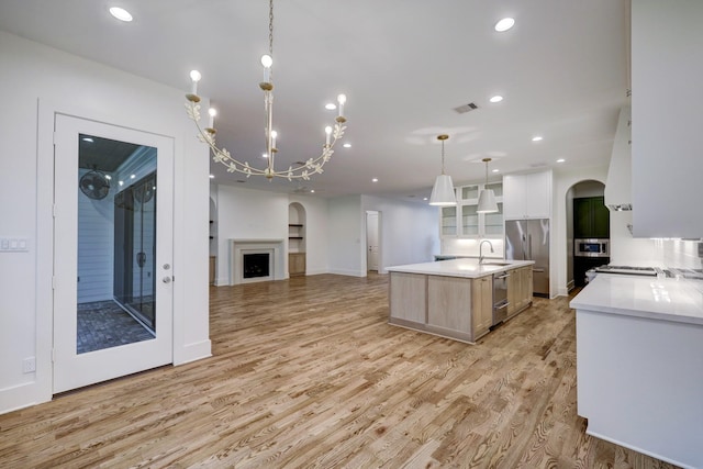 kitchen featuring light wood-type flooring, sink, a large island with sink, white cabinets, and hanging light fixtures