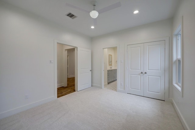 unfurnished bedroom with light carpet, ensuite bath, ceiling fan, multiple windows, and a closet