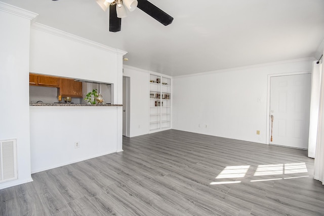 unfurnished living room featuring ceiling fan, built in shelves, crown molding, and light hardwood / wood-style flooring