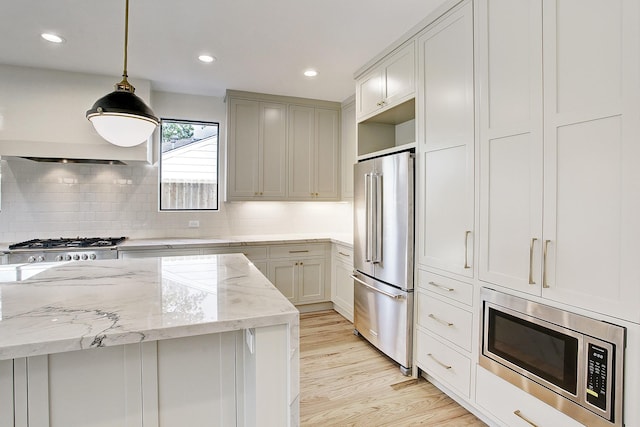 kitchen with decorative backsplash, light stone counters, stainless steel appliances, decorative light fixtures, and light hardwood / wood-style flooring