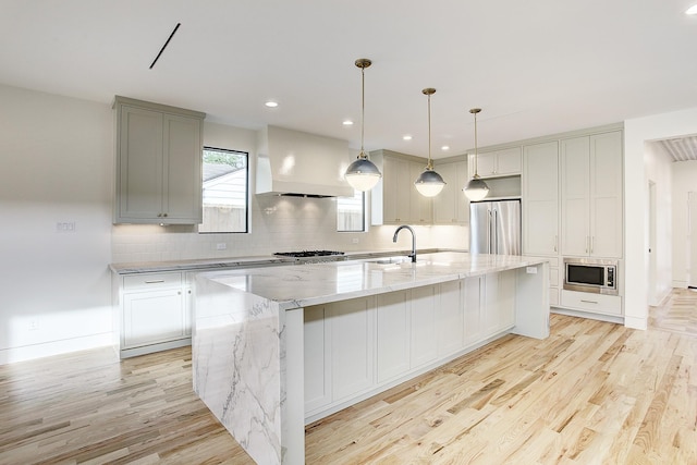 kitchen featuring light stone counters, a spacious island, decorative light fixtures, custom range hood, and appliances with stainless steel finishes