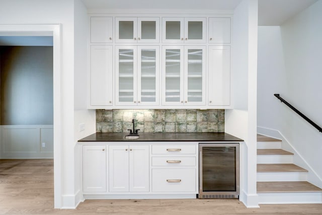 bar featuring backsplash, white cabinetry, beverage cooler, and light hardwood / wood-style floors