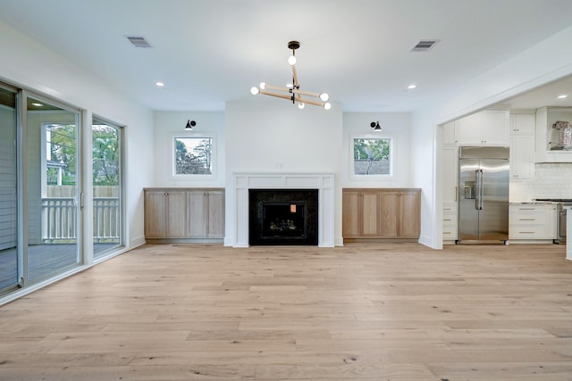 unfurnished living room with a fireplace, light wood-type flooring, a chandelier, and a healthy amount of sunlight