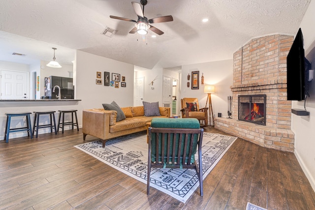 living room featuring ceiling fan, a brick fireplace, hardwood / wood-style floors, lofted ceiling, and a textured ceiling