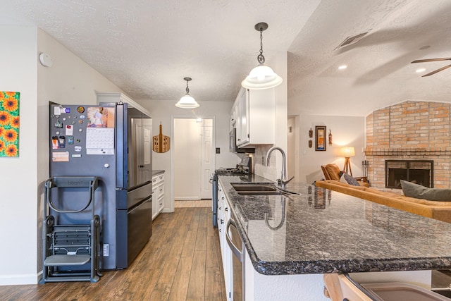 kitchen with a textured ceiling, stainless steel appliances, decorative light fixtures, white cabinets, and lofted ceiling