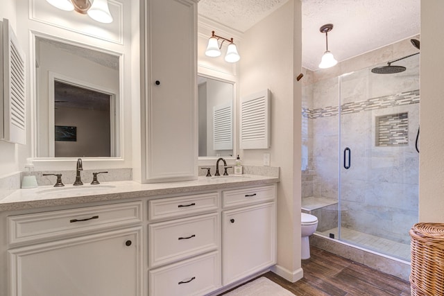 bathroom with hardwood / wood-style floors, a textured ceiling, toilet, vanity, and a shower with shower door