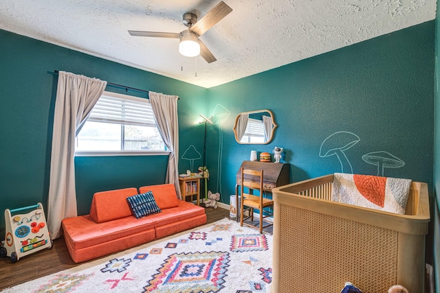 bedroom with ceiling fan, wood-type flooring, a textured ceiling, and a nursery area