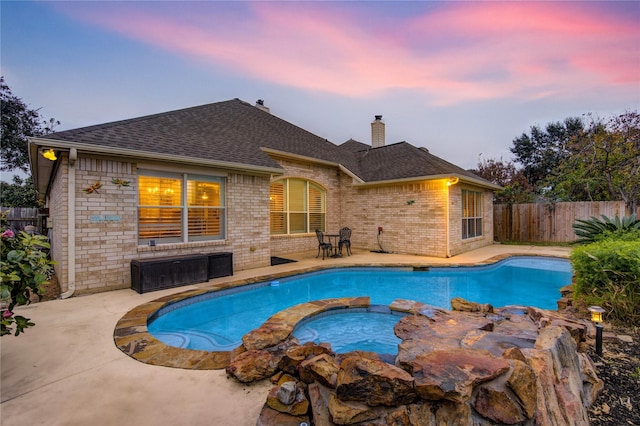 pool at dusk with an in ground hot tub and a patio