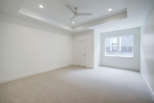 empty room featuring light colored carpet, a raised ceiling, and ceiling fan