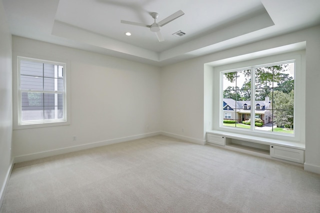 empty room featuring light colored carpet, a raised ceiling, and ceiling fan