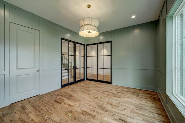 spare room with a wealth of natural light, a notable chandelier, and light wood-type flooring