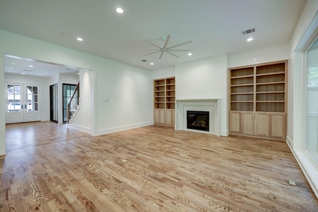 unfurnished living room featuring built in shelves, ceiling fan, light wood-type flooring, and french doors