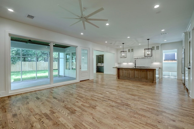 unfurnished living room featuring light wood-type flooring, ceiling fan, and sink