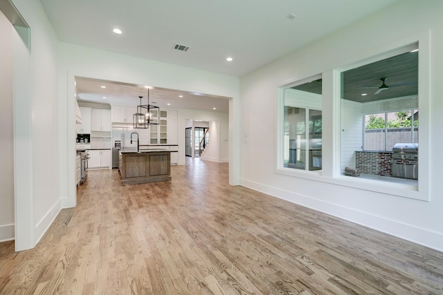 unfurnished living room featuring ceiling fan with notable chandelier, light wood-type flooring, and a wealth of natural light