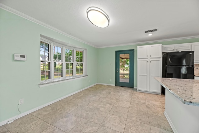 kitchen featuring light stone counters, black refrigerator, white cabinets, and ornamental molding