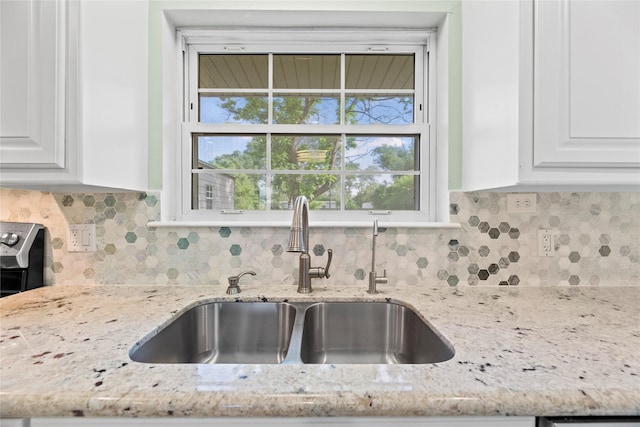 kitchen featuring light stone counters, white cabinetry, sink, and tasteful backsplash