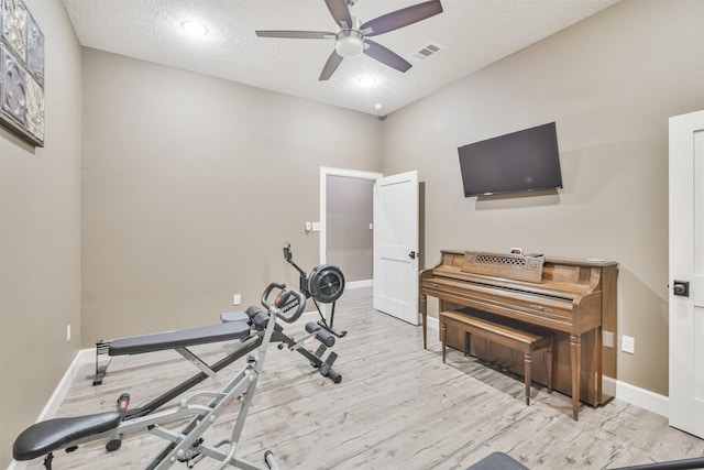 exercise area featuring ceiling fan, light hardwood / wood-style floors, and a textured ceiling