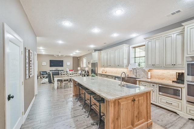 kitchen featuring light stone countertops, sink, stainless steel appliances, a kitchen island with sink, and a breakfast bar