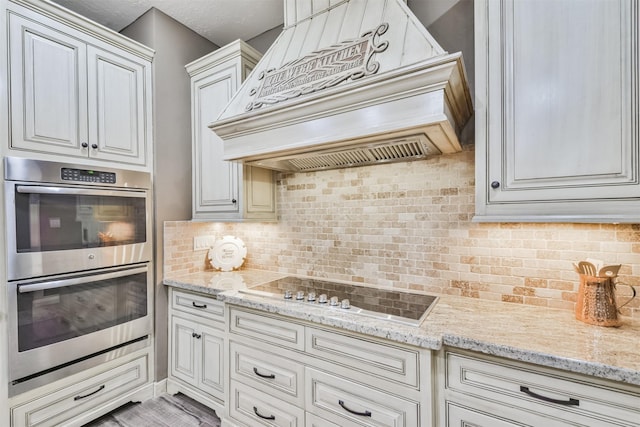 kitchen featuring tasteful backsplash, light stone counters, double oven, stovetop, and custom exhaust hood