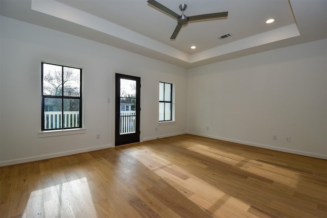 spare room with a tray ceiling, ceiling fan, and light wood-type flooring