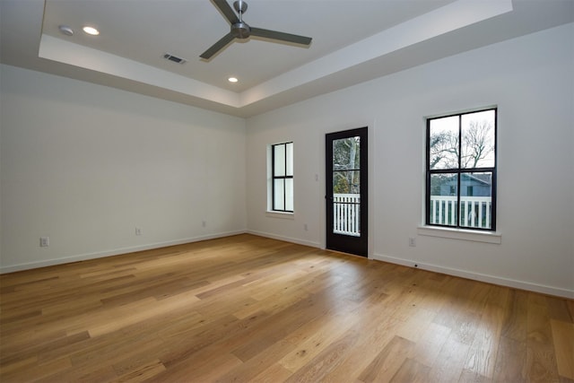 unfurnished room featuring ceiling fan, light hardwood / wood-style flooring, and a tray ceiling