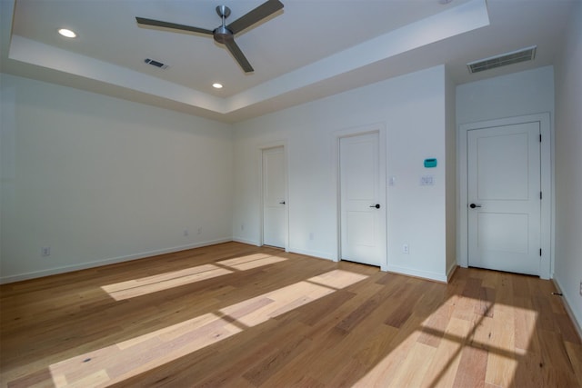 unfurnished bedroom featuring a raised ceiling, ceiling fan, and light wood-type flooring