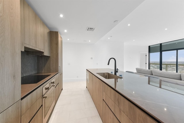 kitchen featuring light stone countertops, sink, backsplash, oven, and black electric cooktop