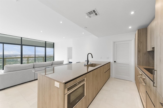 kitchen with light stone countertops, sink, an island with sink, and black electric stovetop