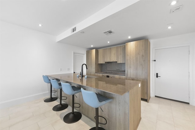 kitchen featuring sink, a kitchen breakfast bar, backsplash, an island with sink, and electric cooktop